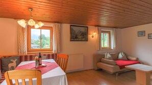 Une pièce chaleureuse avec un plafond en bois, une table à manger avec des chaises, un canapé et une petite table recouverte d’un plaid rouge.