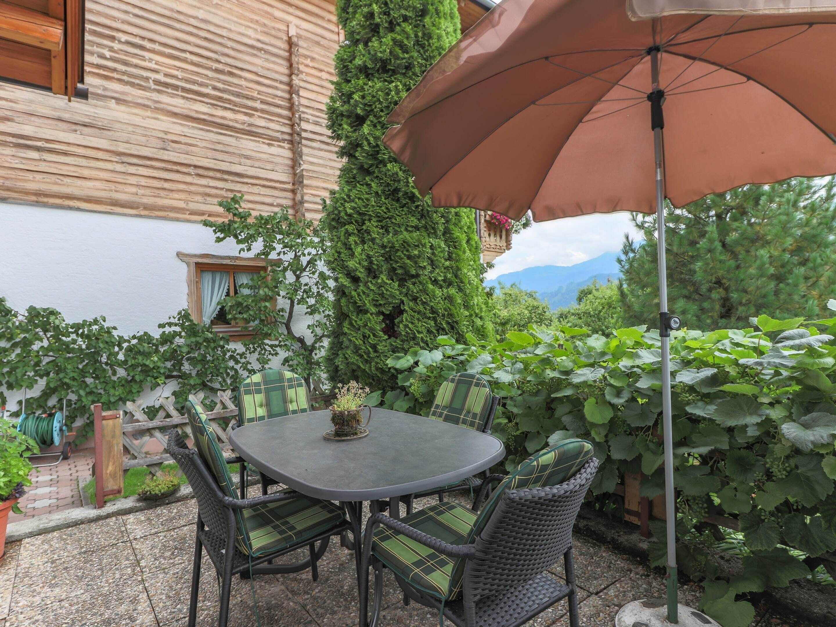 A patio with a round table and chairs, surrounded by greenery and a view of mountains.