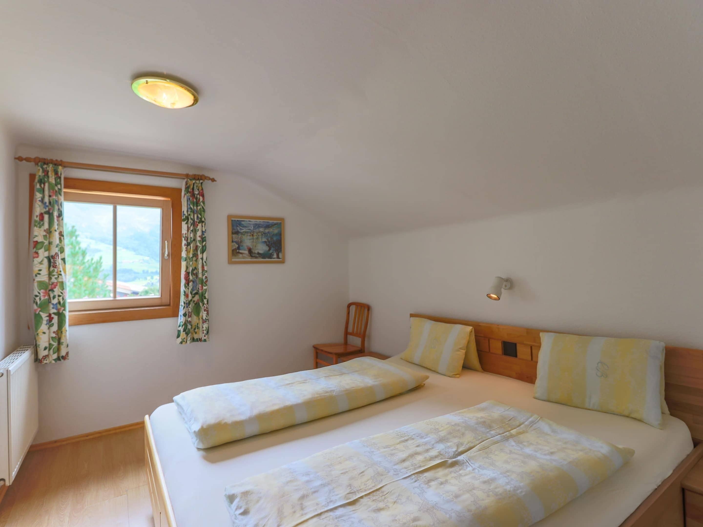 Une chambre à coucher avec un lit, une chaise, une fenêtre avec des rideaux, un tableau et un luminaire au plafond.
