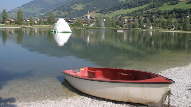Un bateau sur un lac paisible, avec une petite ville et des montagnes en arrière-plan.
