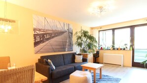 A living room with a sofa, a coffee table, a potted plant, and a large window with a view. - Apartment Niedernsill Near Ski Slopes (Niedernsill)