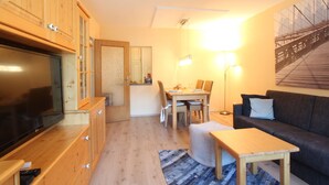 A cozy living room with a TV, wooden cabinets, a dining area with a table and chairs, and a couch. - Apartment Niedernsill Near Ski Slopes (Niedernsill)