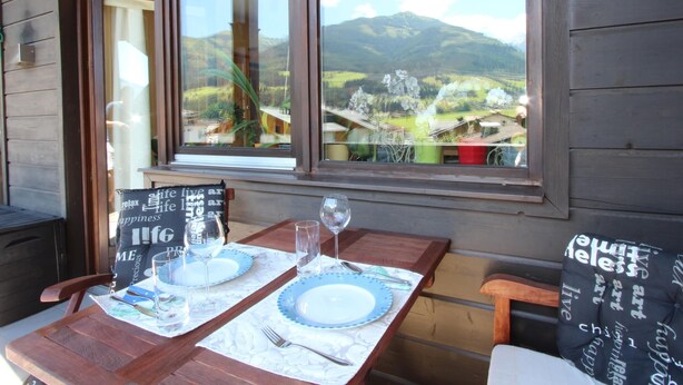 A wooden table set with plates, glasses, and cutlery, with a mountain view through a window. - Apartment Niedernsill Near Ski Slopes (Niedernsill)