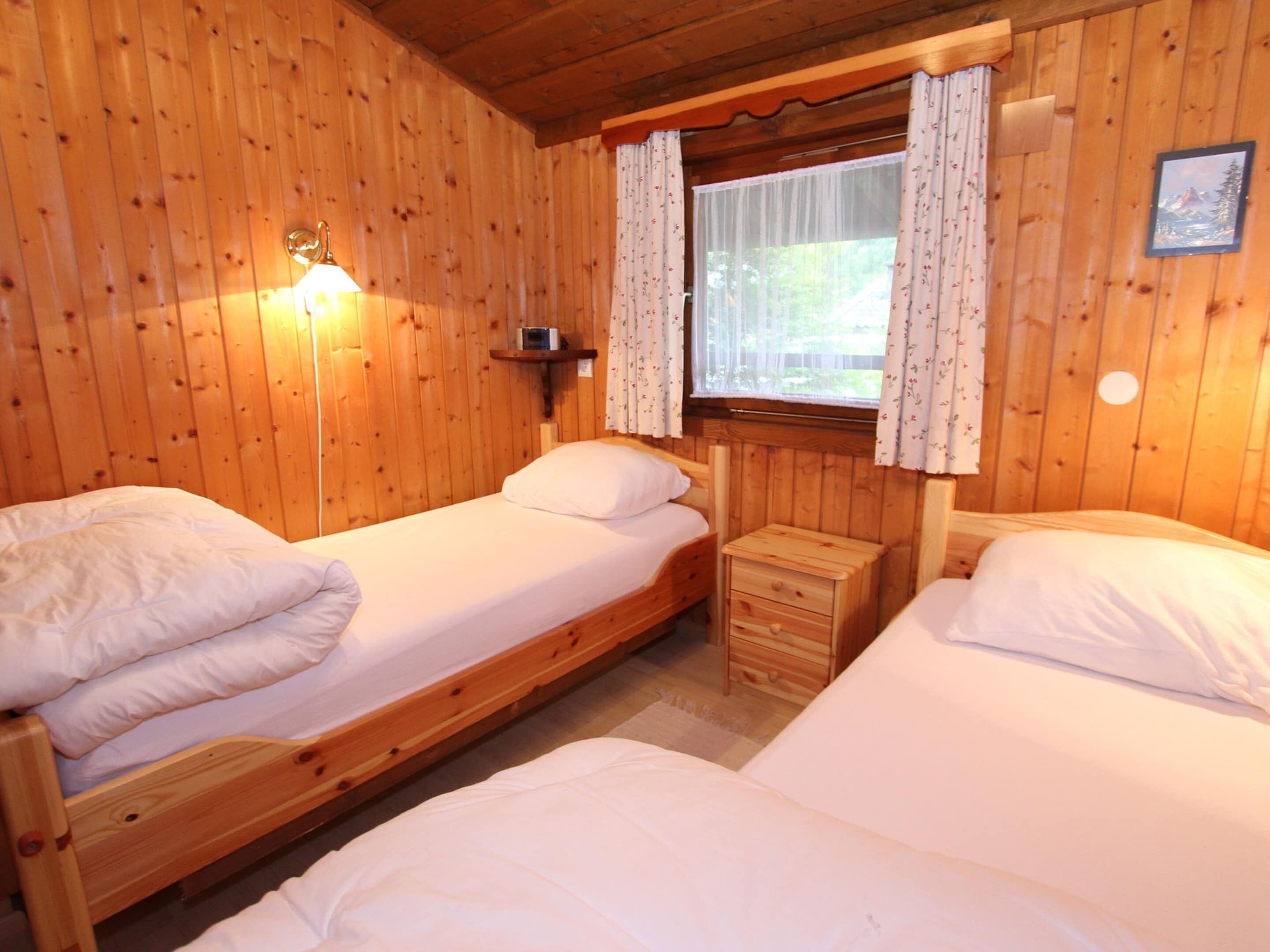 Une cabine équipée de deux lits superposés en bois, d’une petite table de chevet, d’une lampe fixée au mur et d’une fenêtre avec des rideaux.