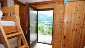 Ein Holzhütten-Zimmer mit Etagenbett, einer Glasschiebetür, die auf einen Balkon führt, und Blick auf eine Berglandschaft.