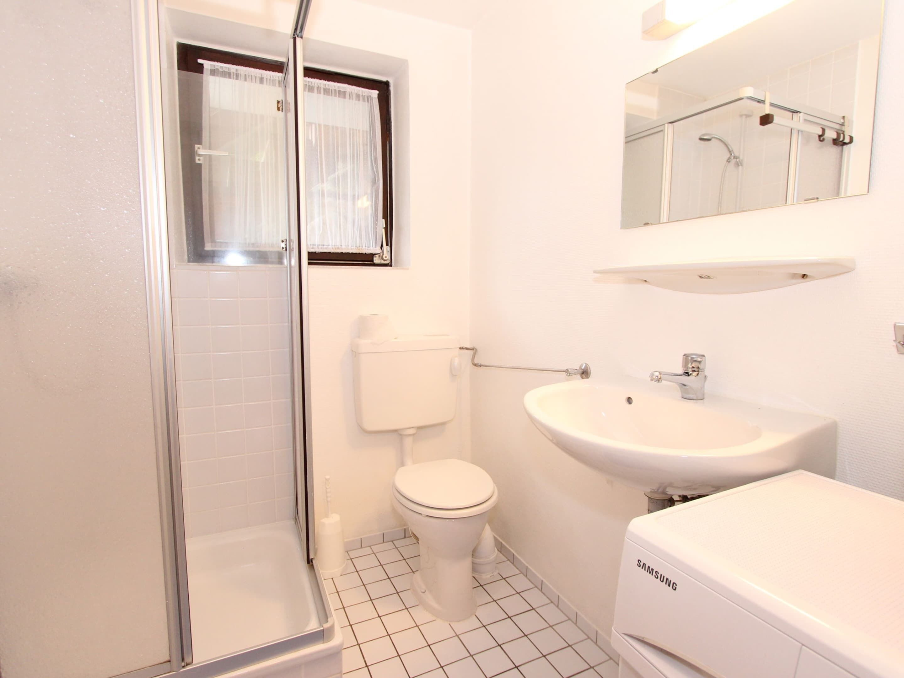 Un baño con ducha, inodoro, lavamanos y un espejo sobre el lavamanos.
