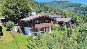 Eine Holzchalet mit Balkon, umgeben von üppigem Grün und Bergen.