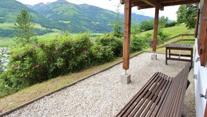 Eine Holzupergola mit einer Bank und einem Tisch, mit Blick auf einen Fluss und grüne Hügel.