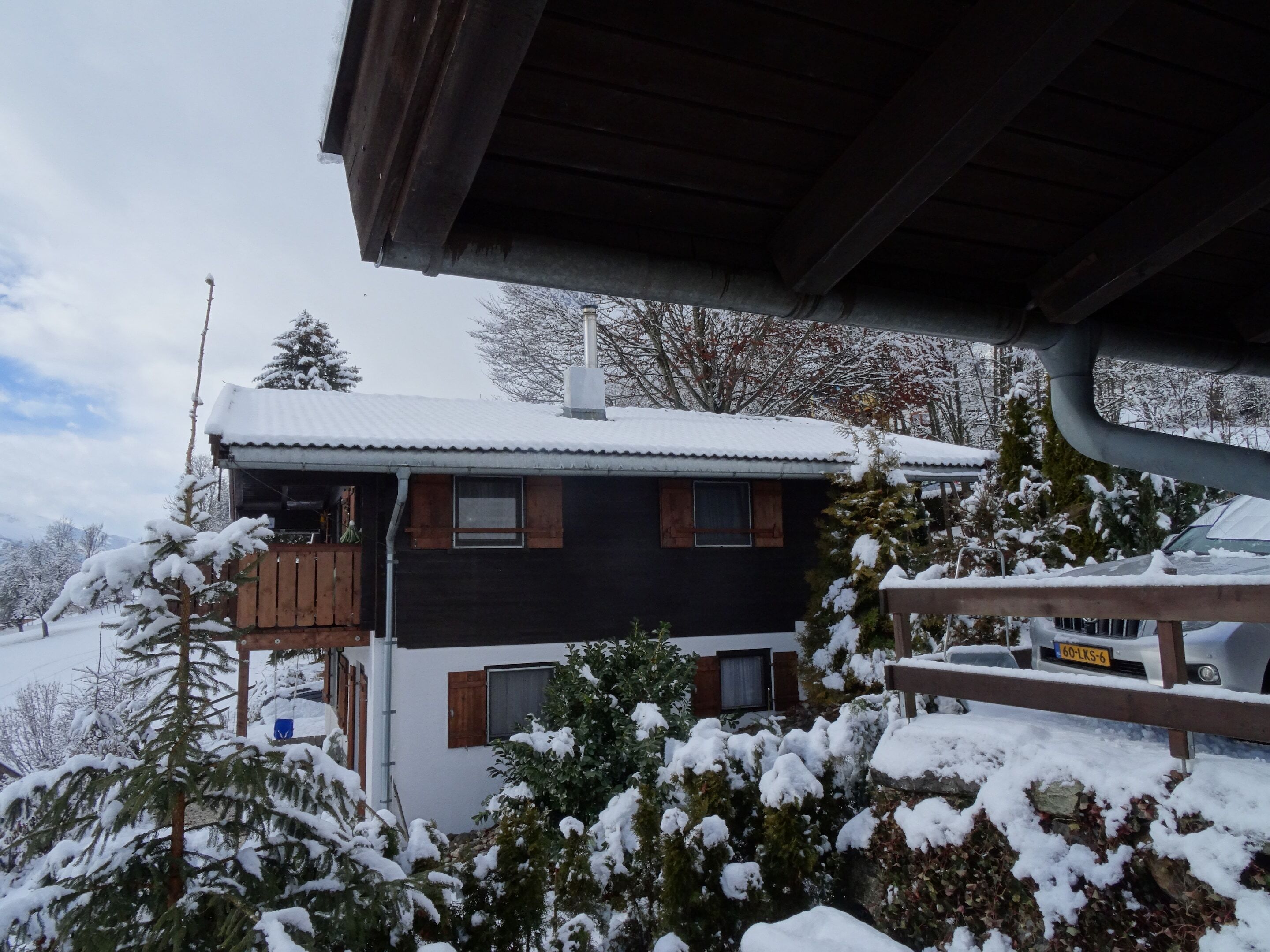 Una cabaña de dos pisos con tejado cubierto de nieve, fachada de madera y un balcón.