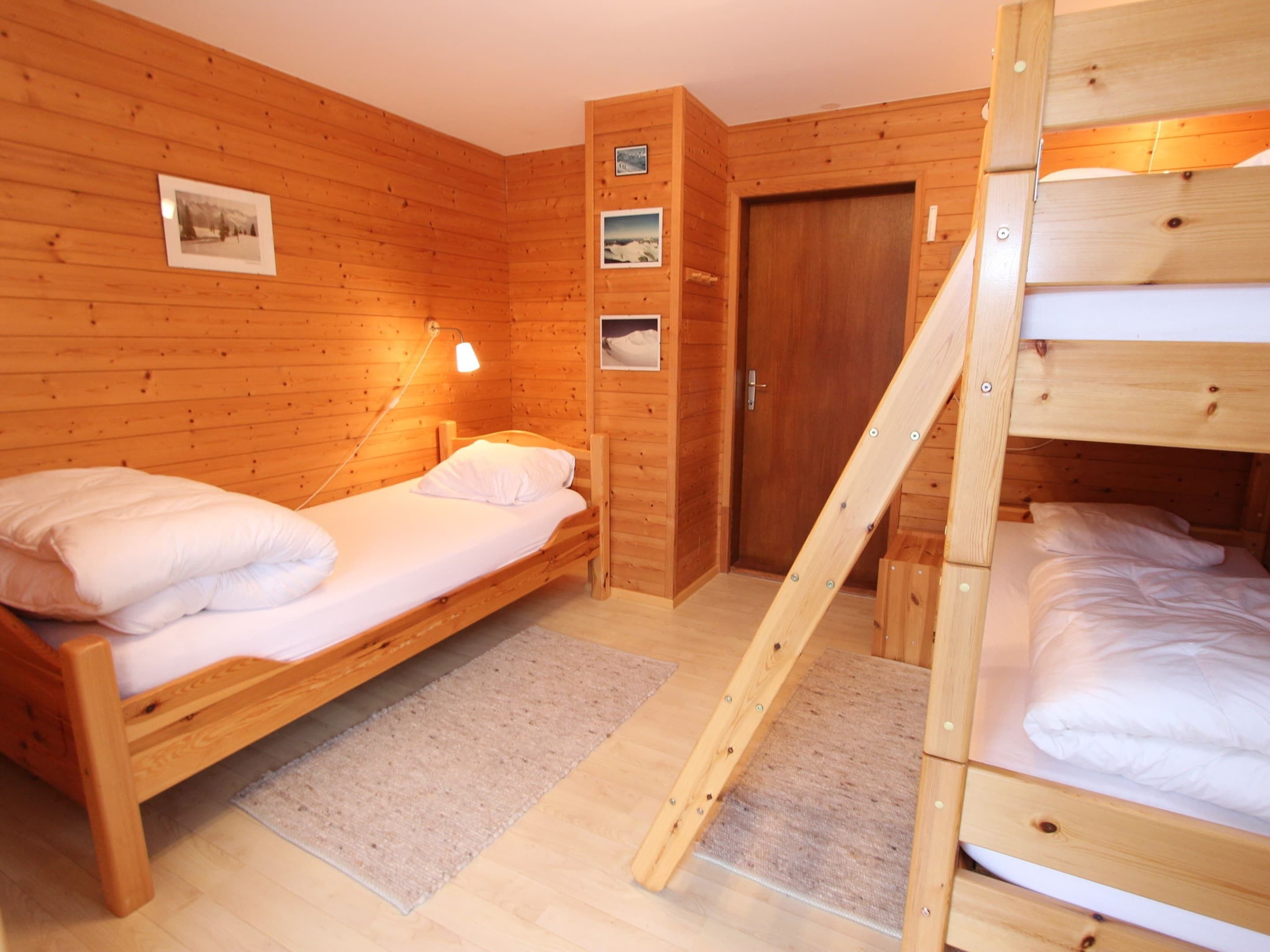 A wooden cabin room with two beds, a door, and a wall-mounted lamp.