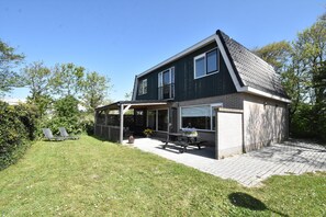 A two-story house with a patio area, a covered seating area, and a garden.
