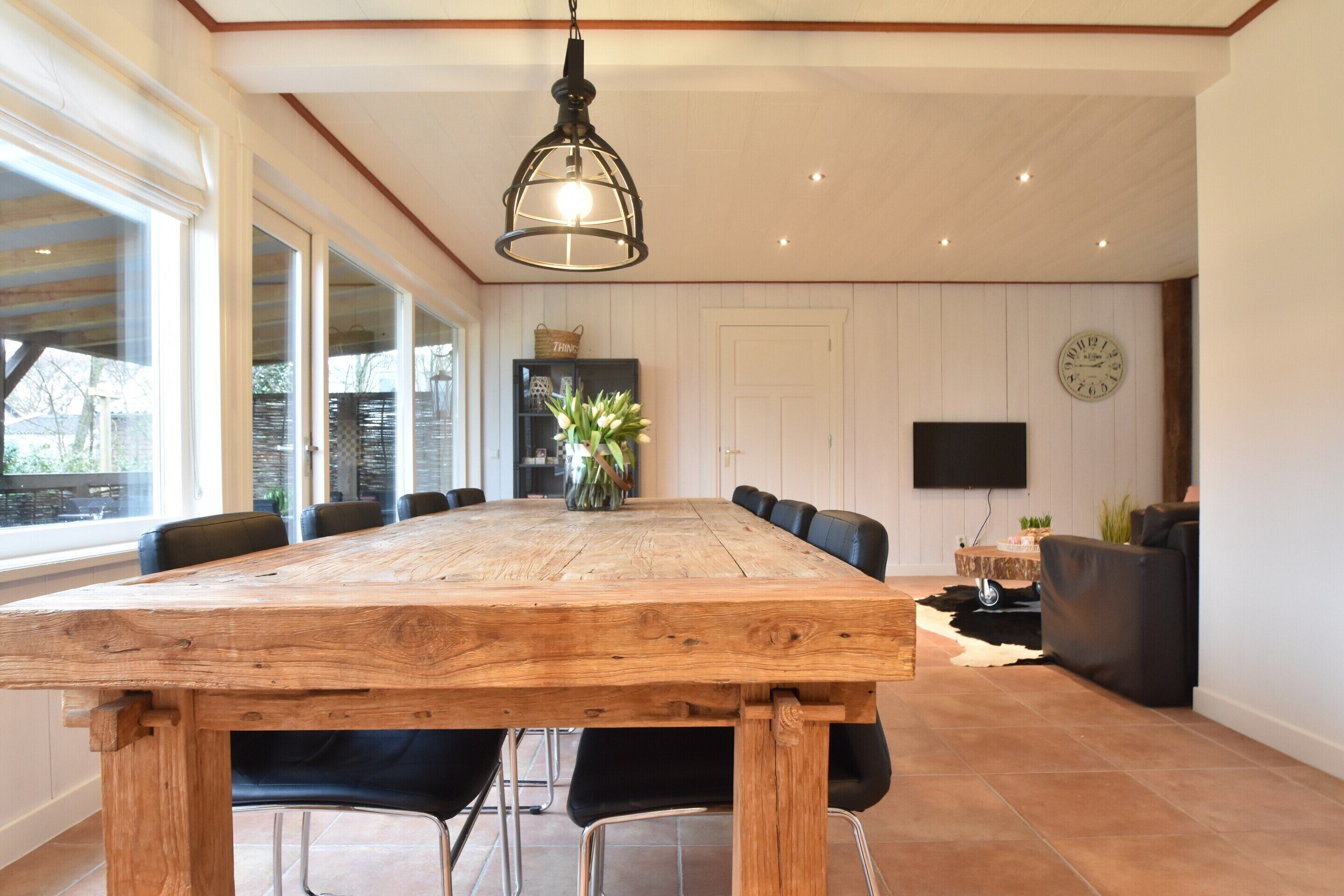 A spacious dining area with a large wooden table, black chairs, and a hanging light fixture.