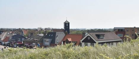Uma cidade com uma torre de igreja imponente, diversos edifícios residenciais e um primeiro plano gramado.