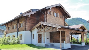 A two-story wooden house with a covered porch and a small garden area. - Apartment in Hollersbach Near Ski Lift (Hollersbach im Pinzgau)
