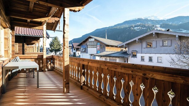 A wooden balcony with a table and chairs, overlooking a village with traditional houses and mountains in the background. - Apartment in Hollersbach Near Ski Lift (Hollersbach im Pinzgau)