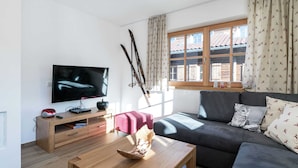 A modern living room with a flat-screen TV, wooden furniture, a sofa, and a window with patterned curtains. - Apartment in Hollersbach Near Ski Lift (Hollersbach im Pinzgau)