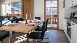 A modern kitchen with a dining area, wooden ceiling beams, and a view of a snowy landscape through a glass door. - Apartment in Hollersbach Near Ski Lift (Hollersbach im Pinzgau)
