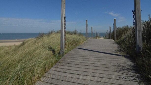 A wooden boardwalk leading to a beach, surrounded by tall grass and wooden posts. - Holiday Home Koewacht Near Seaside (Koewacht)