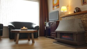 A living room with a fireplace, a television on a stand, a leather chair, and a table with candles. - Holiday Home Koewacht Near Seaside (Koewacht)