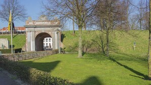 A historic stone archway with a plaque, surrounded by a grassy area and trees. - Holiday Home Koewacht Near Seaside (Koewacht)