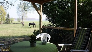 A covered outdoor seating area with a table and chairs, overlooking a grassy field with horses. - Holiday Home Koewacht Near Seaside (Koewacht)