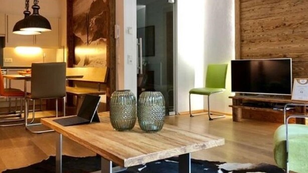 A modern living room with a wooden dining table, a green armchair, and a television.
