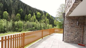 A balcony with a stone wall and a wooden fence overlooking a forested valley.