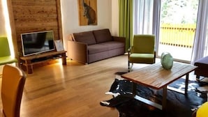 A living room with a wooden wall, a sofa, a chair, a coffee table, and a TV.