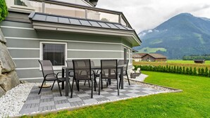Een modern huis met een patio, compleet met een tafel en stoelen, omgeven door een verzorgd gazon en een berg op de achtergrond.
