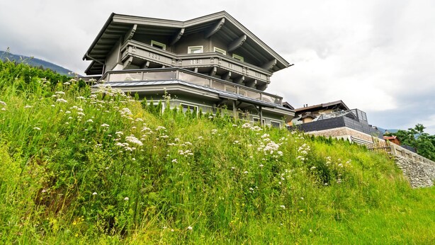 Een meerlaags gebouw met balkons, gelegen op een groene heuvel vol bloemen.