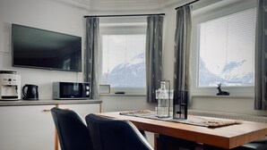 Een moderne keuken met een flatscreen-tv, koffiezetapparaat, magnetron en een eethoek met twee stoelen en een tafel.