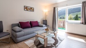 Un salón moderno con un sofá gris, una mesa de centro de cristal y vistas a un paisaje verde a través de un gran ventanal.