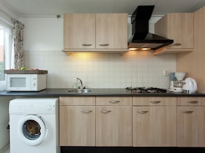A compact kitchen with a washing machine, a microwave, a sink, a stove, and wooden cabinets.