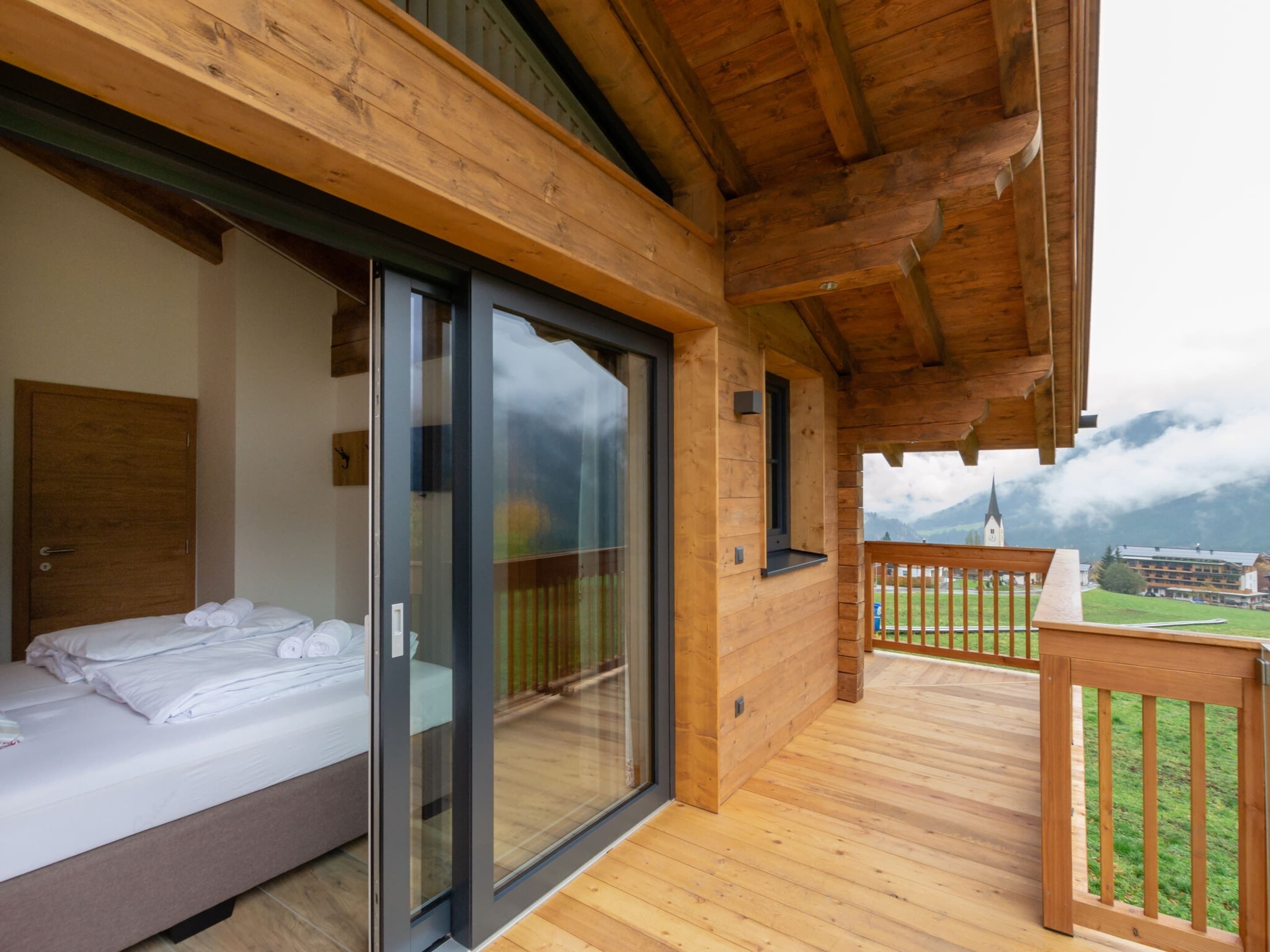 A wooden balcony with a bed and sliding glass doors leading to a room.