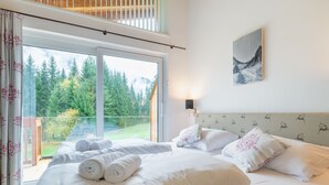 Hotellihuone, jossa on suuri sänky, näkymä puihin ja vuorille sekä taulu seinällä.