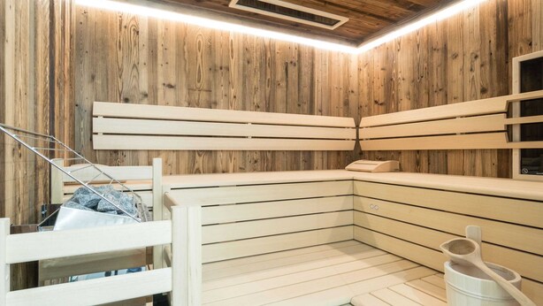 Eine Sauna mit Holzwänden und -bänken, eine Holzbank mit Handtuch sowie ein Holzeimer mit Wasserschöpfkelle.