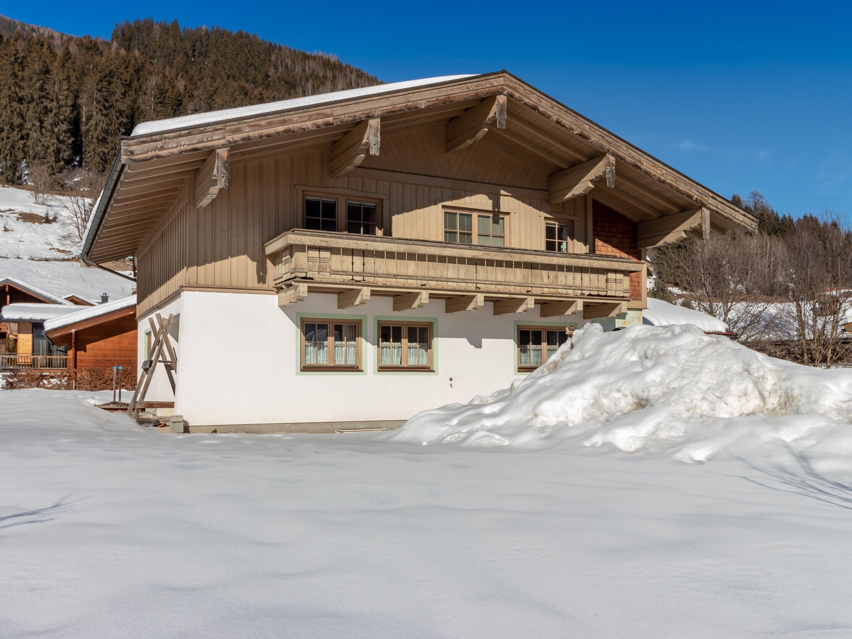 Een chalet met houten gevel, een balkon en een met sneeuw bedekte grond.