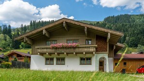 Un chalet traditionnel doté d’un balcon, entouré d’une végétation luxuriante et offrant une vue sur un paysage montagneux.