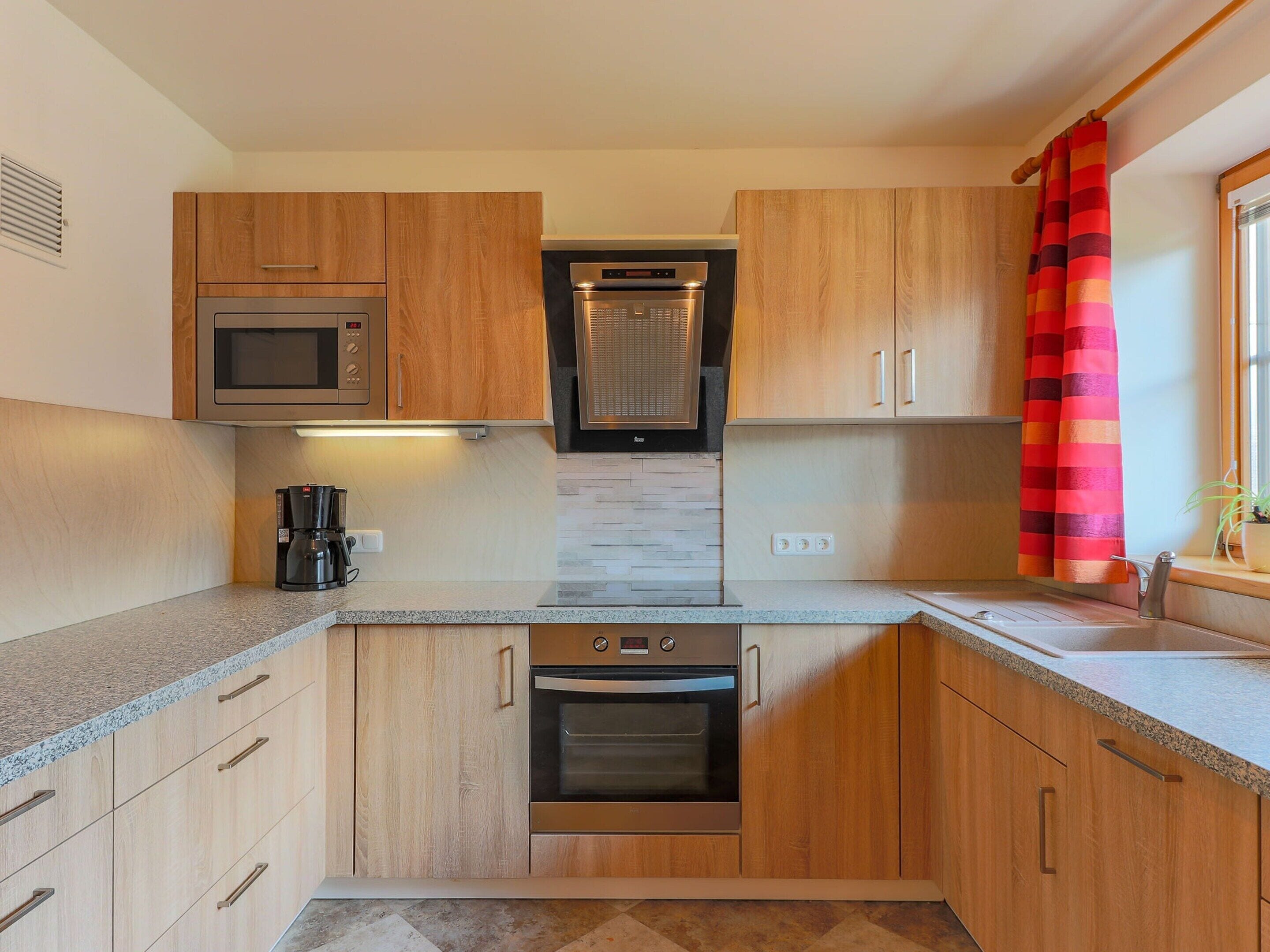 A modern kitchen with wooden cabinets, a built-in oven, a microwave, and a coffee maker.