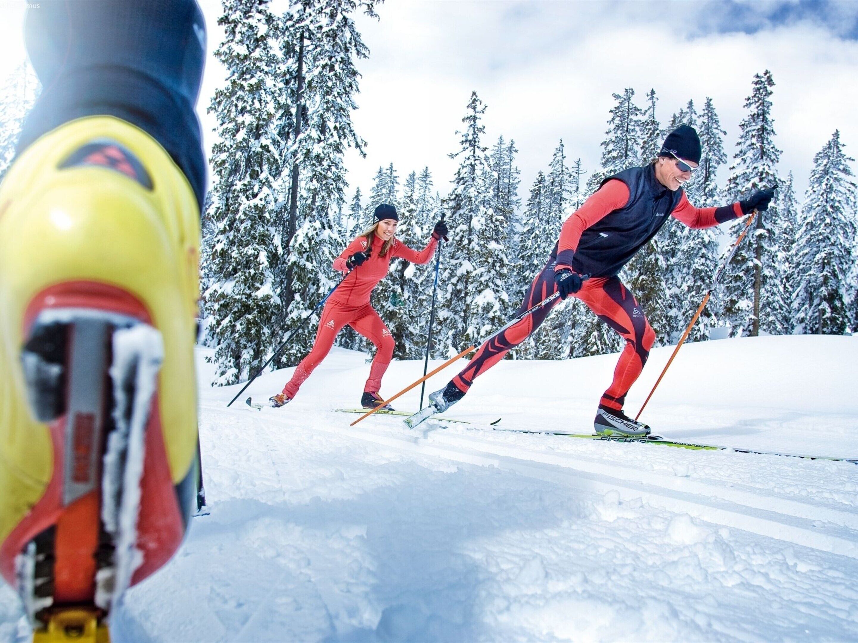 En person som åker skidor i en snötäckt sluttning med träd i bakgrunden.