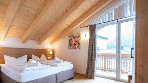 Une chambre avec un plafond en bois, un lit recouvert de draps blancs, un tableau accroché au mur et un balcon avec vue.
