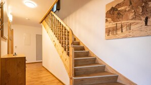Un escalier en bois avec une rampe, un comptoir d’accueil en bois et un tableau représentant un paysage enneigé accroché au mur.