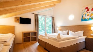 Une chambre confortable avec un grand lit, une petite table de chevet, un téléviseur fixé au mur et une fenêtre avec des rideaux.