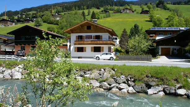 A chalet with a white car parked in front, surrounded by a river and greenery. - Luxury Chalet with Sauna near Ski Area in Salzburg (Saalbach-Hinterglemm)