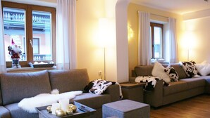A living room with a grey sofa, a smaller grey armchair, and a coffee table with Christmas decorations. There are two windows with curtains, and a balcony with a railing is visible through the windows. - Luxury Chalet with Sauna near Ski Area in Salzburg (Saalbach-Hinterglemm)