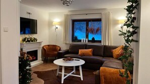 A living room with a fireplace, a sofa, a coffee table, and a television. - Luxury Chalet with Sauna near Ski Area in Salzburg (Saalbach-Hinterglemm)