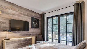 A modern bedroom with a large bed, a mounted TV, a wooden desk, and a view of the outdoors through large windows. - Chalet in Krimml Near Zillertal Ski Arena (Krimml)