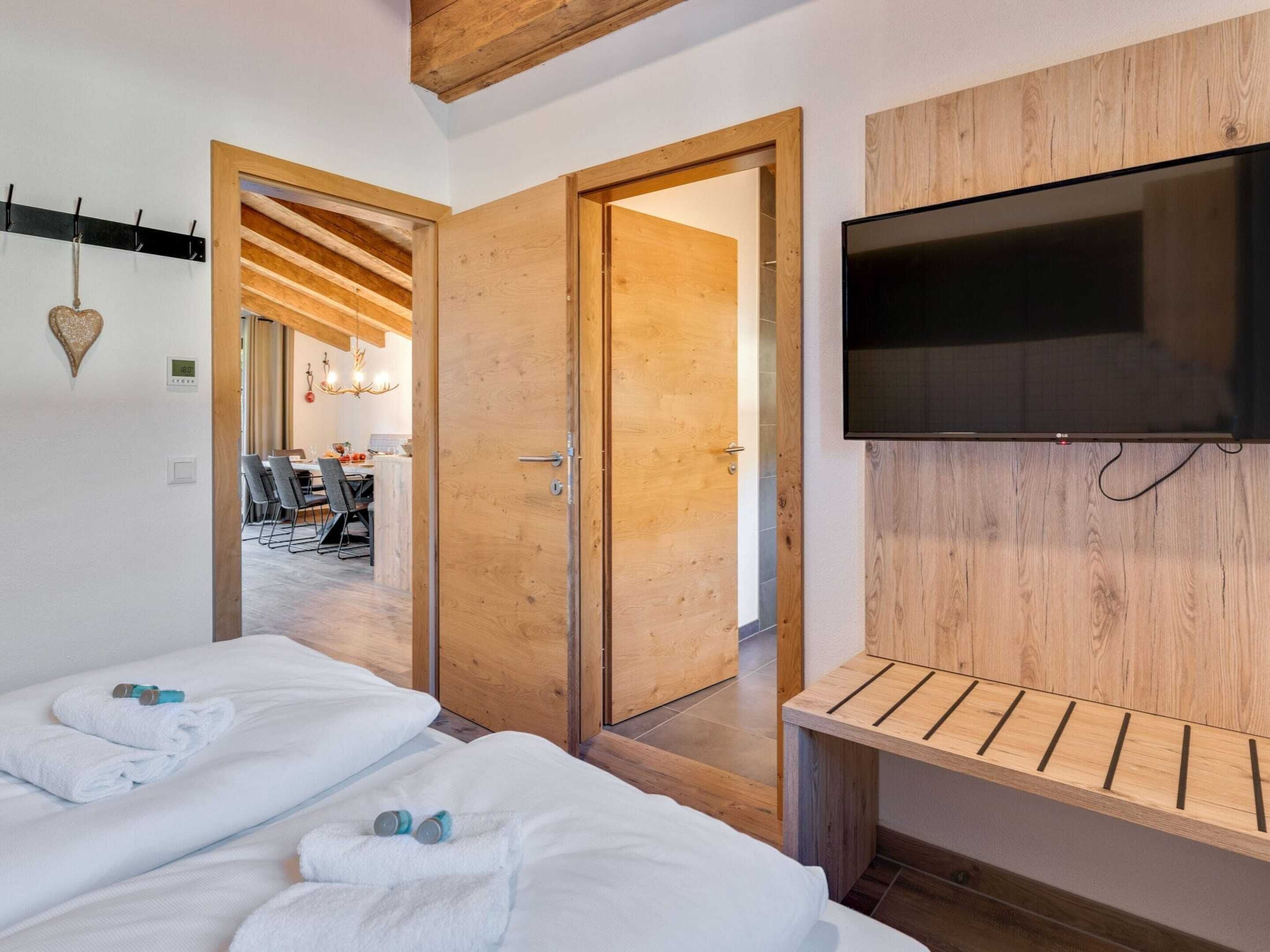 A hotel room with two beds, a TV, wooden paneling, and a dining area visible through an open door.
