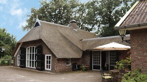 A traditional thatched-roof house with a brick exterior, large windows, and a patio area with a table and chairs.