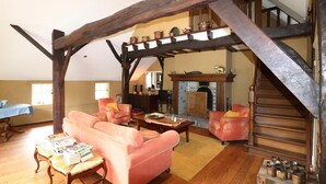 A spacious living room with a high wooden ceiling, a fireplace, and a staircase leading to an upper level.